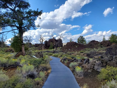 A winding path through a rocky landscape with sparse vegetation and a blue sky dotted with clouds.