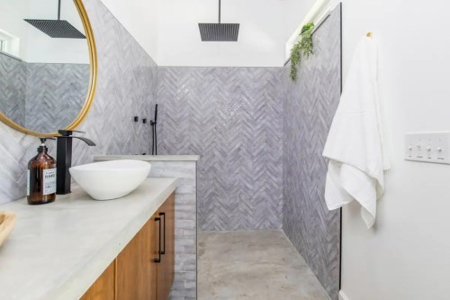 Modern bathroom featuring herringbone tile, a round mirror, a sleek sink, and a minimalist design.