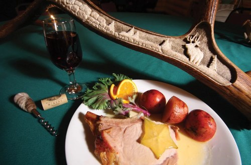 A plate with turkey, potatoes, and garnish, alongside a glass of red wine and a decorative antler.