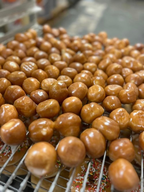 A close-up of freshly glazed doughnut holes cooling on a wire rack, with colorful sprinkles in the background.