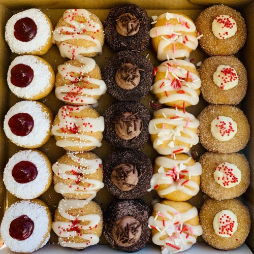 A box of assorted cupcakes with various toppings, including sprinkles, frosting, and fruit preserves.