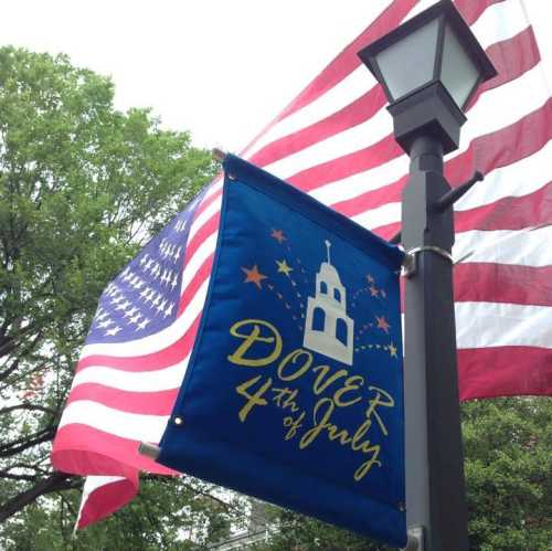 A blue banner reading "DOVER 4th of July" hangs beside an American flag on a lamppost, with trees in the background.