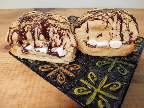 Two halves of a pastry filled with marshmallows and drizzled with chocolate, served on a decorative plate.
