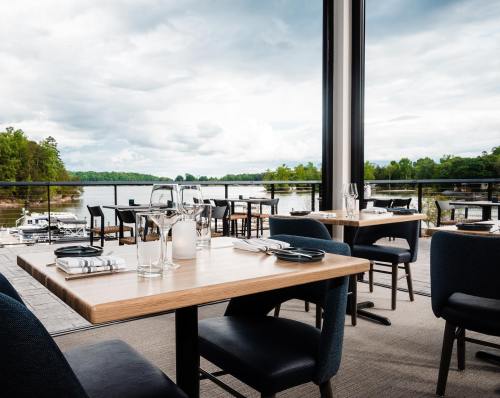 A modern restaurant with wooden tables and chairs, overlooking a scenic waterfront view through large windows.