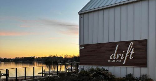 A lakeside building with a sign reading "drift" at sunset, reflecting calm waters and a serene atmosphere.