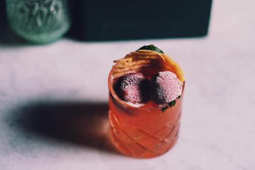 A vibrant cocktail garnished with strawberries and mint, served in a textured glass on a marble surface.