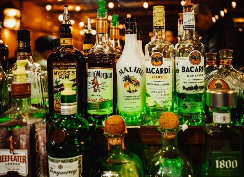 A variety of liquor bottles displayed on a bar shelf, including rum, vodka, and tequila.