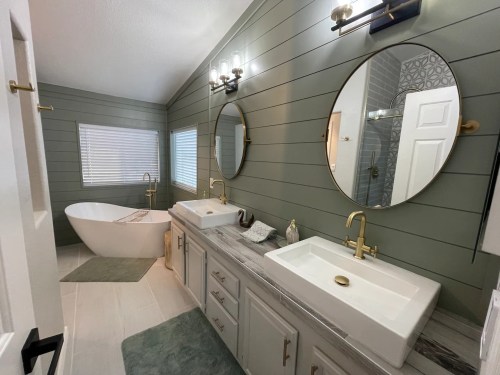 Modern bathroom featuring a freestanding tub, dual sinks, round mirrors, and green shiplap walls. Bright and stylish design.