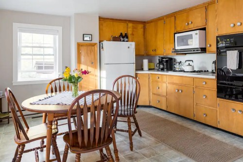 Cozy kitchen with wooden cabinets, a dining table, flowers, and appliances including a microwave and coffee maker.
