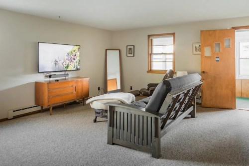 Cozy living room with a TV, mirror, wooden furniture, and a door leading outside. Bright and inviting atmosphere.