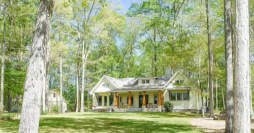 A charming yellow house surrounded by tall trees and greenery on a sunny day.