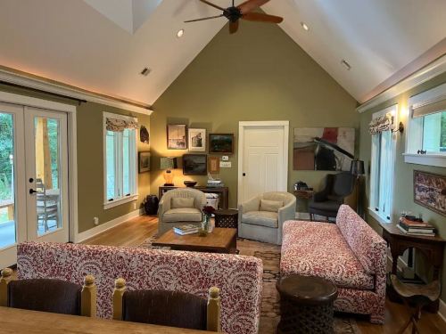 Cozy living room with a high ceiling, green walls, patterned sofas, and natural light from large windows.