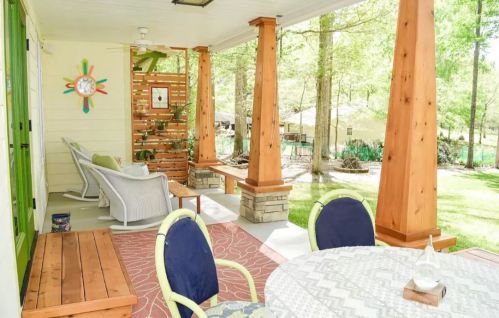 A cozy porch with wooden pillars, a round table, and comfortable seating, surrounded by greenery and a peaceful atmosphere.
