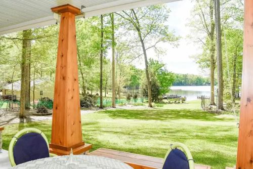 A serene view from a porch overlooking a lake surrounded by trees and greenery.