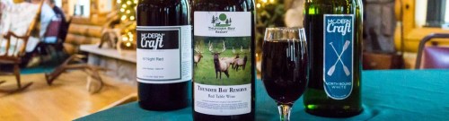 Three bottles of wine on a table, with a glass of red wine in front, set in a cozy, rustic environment.