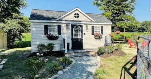 A charming small house with a black door, flower boxes, and a landscaped yard under a clear blue sky.