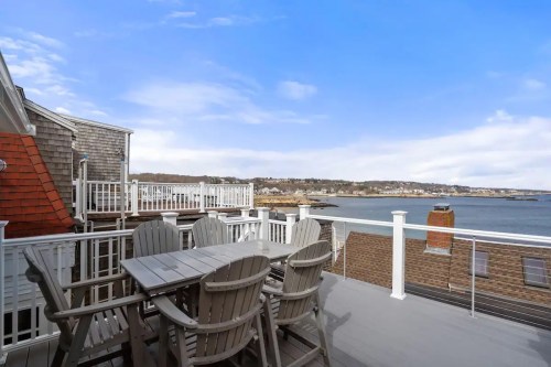 A scenic view from a deck overlooking the ocean, with outdoor seating and a clear blue sky.