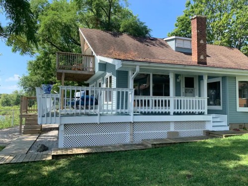 A charming blue house with a porch, surrounded by greenery and a clear blue sky.