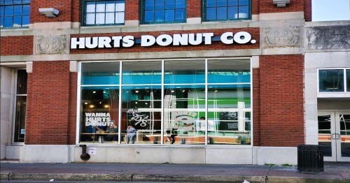 Exterior of Hurts Donut Co. with large windows and a sign, featuring a playful slogan about donuts.