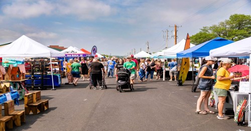 A bustling outdoor market with colorful tents, vendors, and crowds of people shopping and enjoying the day.
