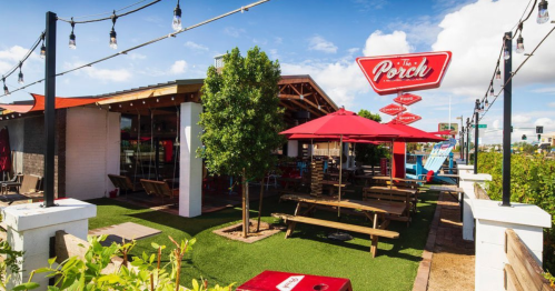 Outdoor dining area of a restaurant called "The Porch," featuring picnic tables, umbrellas, and string lights.