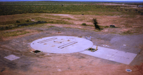 A large, circular concrete launch pad in a barren landscape with sparse vegetation and clear blue skies.