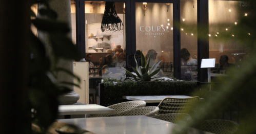A view of a restaurant named "COURSE," with diners visible through large windows and greenery in the foreground.