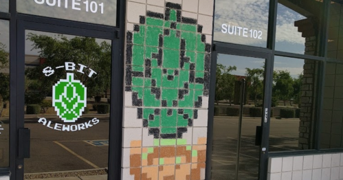 Pixel art of a green plant on a brick wall next to a sign for "8-Bit Aleworks" at a business entrance.