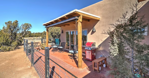 A cozy patio with chairs and a grill, surrounded by desert landscape and trees under a clear blue sky.