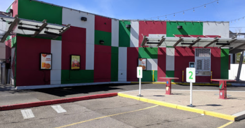 Colorful fast-food restaurant exterior with red and green stripes, featuring two order stations in front.