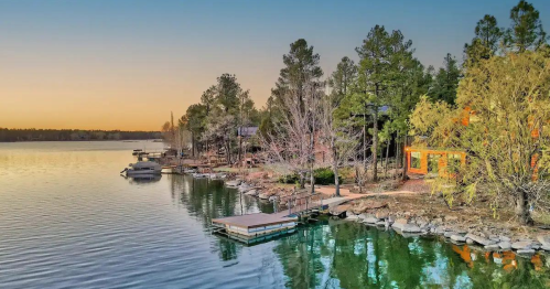 A serene lakeside view at sunset, featuring docks, trees, and calm waters reflecting the colorful sky.