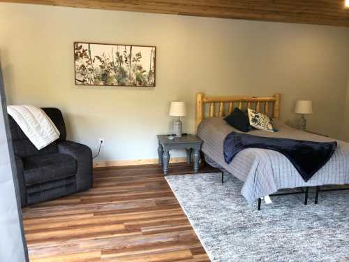 Cozy bedroom featuring a wooden bed, gray bedding, a chair, side tables, and a decorative wall art.