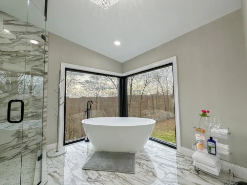 Modern bathroom featuring a freestanding tub, large windows with a scenic view, and elegant marble flooring.