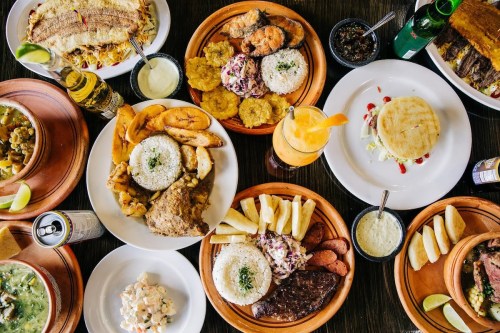 A vibrant spread of various dishes, including rice, fried plantains, seafood, and drinks, arranged on wooden plates.