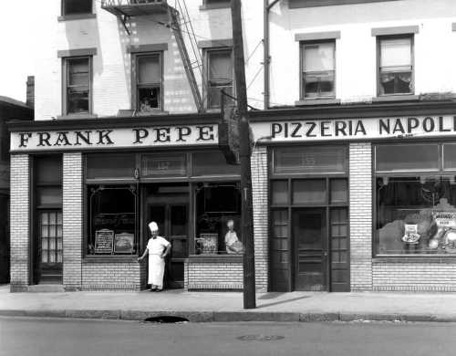 Historic black-and-white photo of Frank Pepe Pizzeria Napoli, featuring a chef outside the restaurant.