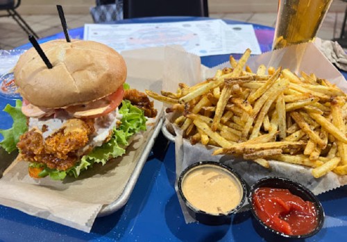 A crispy chicken sandwich with lettuce, tomato, and sauce, served with a side of golden fries and dipping sauces.