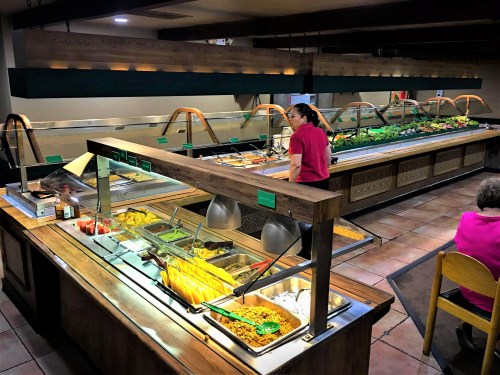 A buffet with various food options, including salads and hot dishes, and a staff member serving customers.