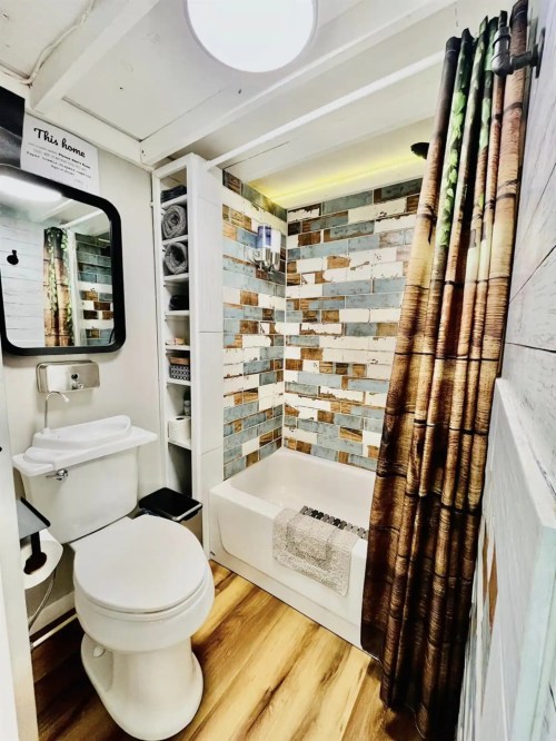 A small bathroom featuring a bathtub, patterned shower curtain, mirror, and colorful tiled walls.