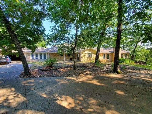 A spacious brick house surrounded by trees, with a driveway leading up to it on a sunny day.
