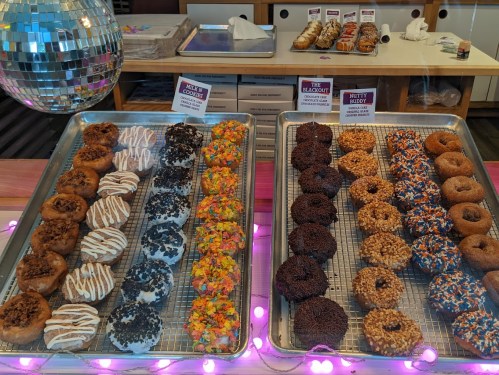 A display of assorted donuts, featuring various toppings and flavors, arranged on trays with a disco ball in the background.