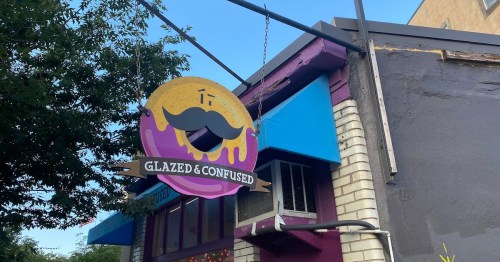 A colorful sign for "Glazed & Confused" featuring a donut with a mustache, hanging outside a shop.