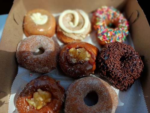 A box of assorted donuts, including glazed, chocolate, and sprinkled varieties, arranged neatly.