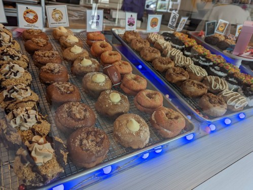 A display of assorted donuts and pastries, featuring various toppings and flavors, arranged on trays.