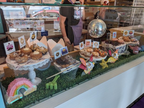 A display case filled with colorful donuts and pastries, decorated with playful signs and a disco ball.