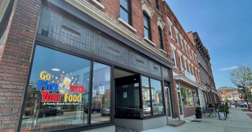 Exterior of a brick building featuring a sign for "Go Play With Your Food," a family board game tavern.