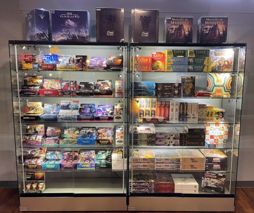 Two glass display cases filled with various board games and card games, showcasing colorful boxes and game components.