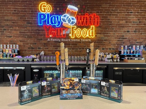 A bar with colorful taps and board games, featuring a neon sign that reads "Go Play with Your Food."