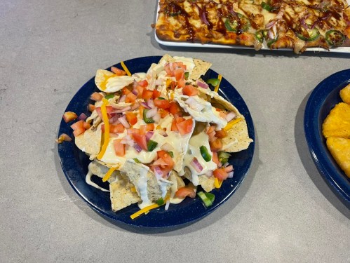 A plate of nachos topped with cheese, tomatoes, jalapeños, and shredded lettuce, served on a blue dish.