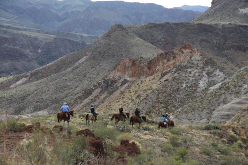 A group of horseback riders traverses a rugged, mountainous landscape with green hills and rocky formations.