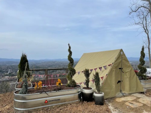 A tan tent set up on a hillside with decorative plants and a scenic view of the landscape in the background.